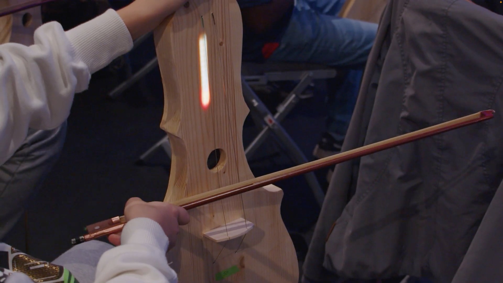 A young person playing a prototypical wooden violin controller and audio device based on Bela hardware during a performance of the play Symphonie at Theatre Straahl in Berlin 2023